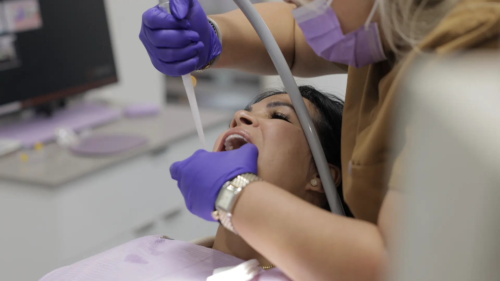 A dental professional treating a patient with dental instruments and suction.