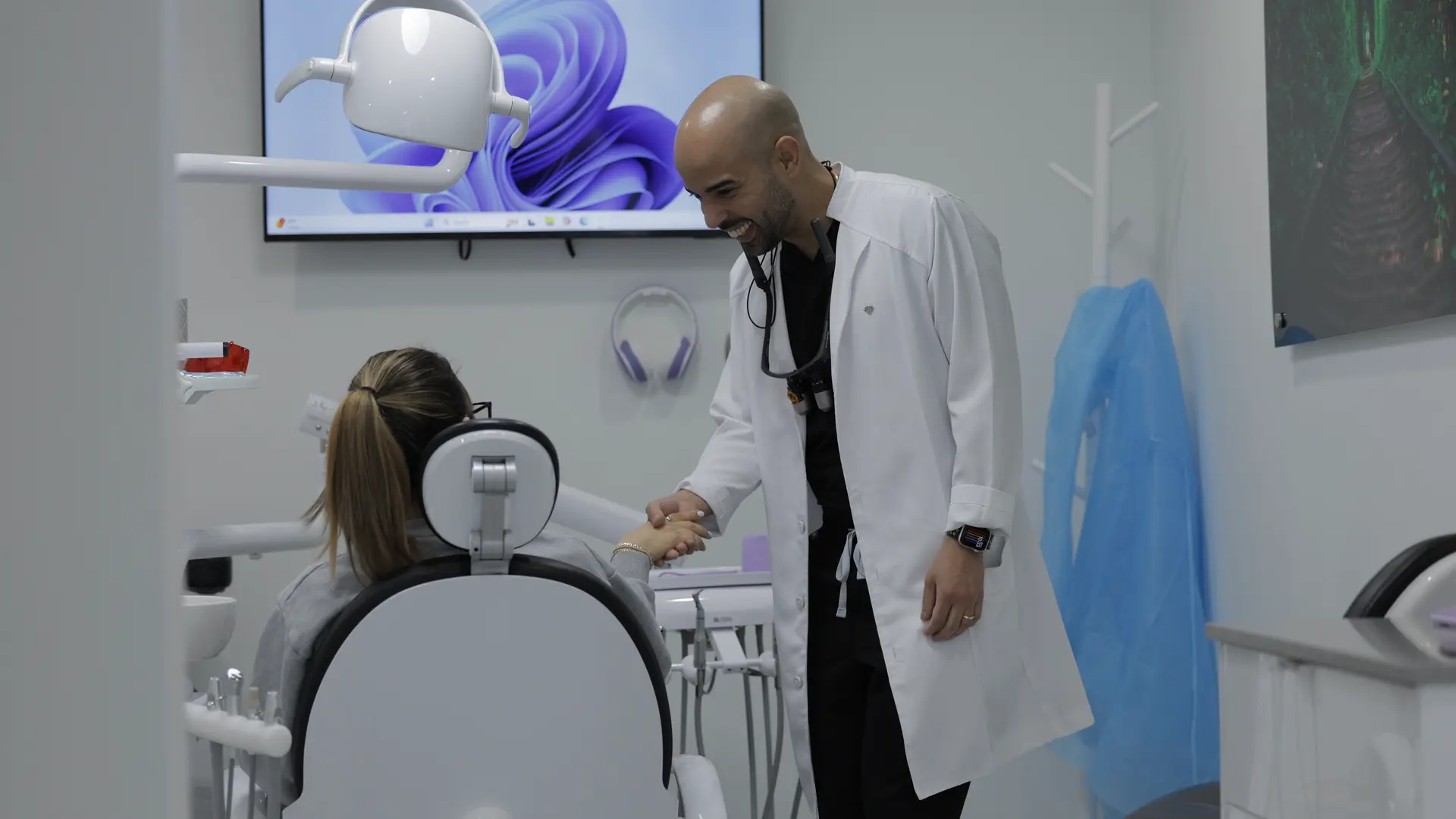 A dentist greeting a seated patient with a handshake.