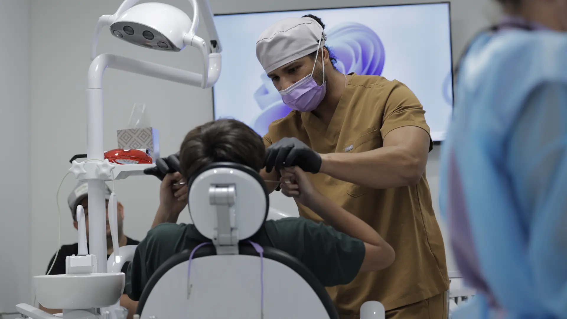 A dental professional preparing a patient for care in a dental chair.