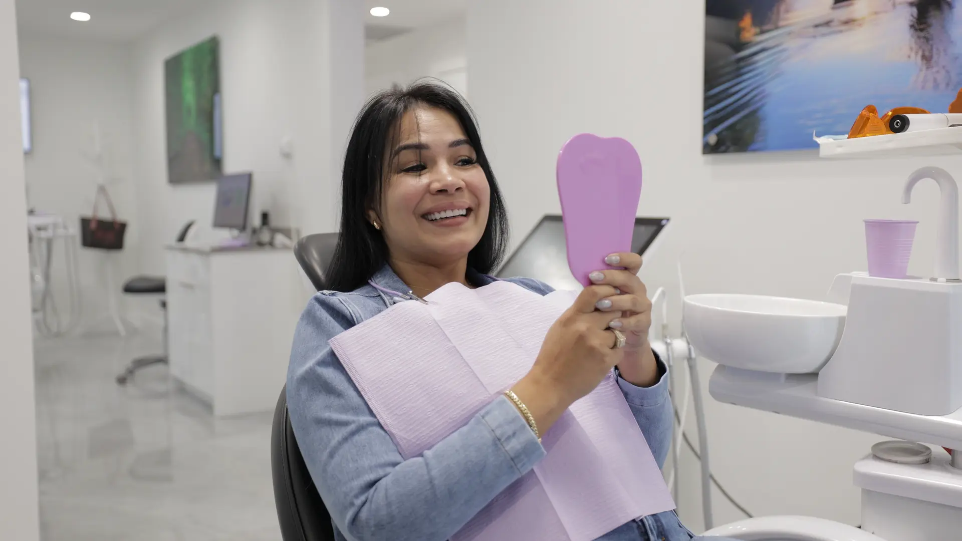 A patient smiling while looking into a handheld mirror in a dental chair.